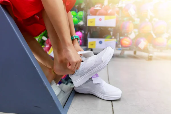 Little girl tried shoe in front of mirror in shopping mall. Asian girl smileing happy to choice and tried sneaker in front of mirror in shop with copy space. Girl holding  sneaker for tried.