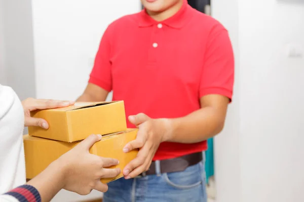 Delivery man delivering package to homeowner. Woman hand accepting a delivery of boxes from deliveryman. Delivery man wear red uniform sent box package to women hand. Delivery concept.