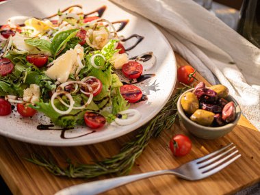 Tahta tabakta çeşitli peynir atıştırmalıkları ve beyaz tabakta salata.