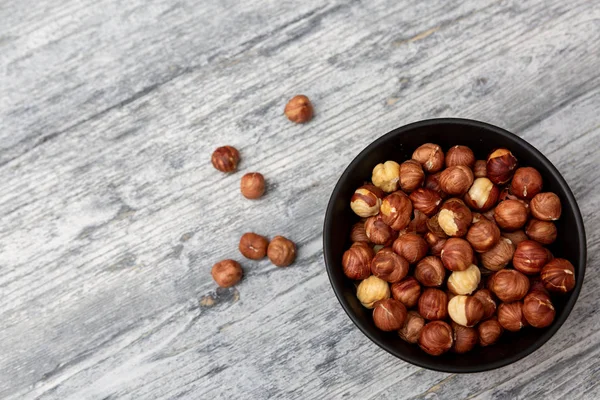 Roasted hazelnuts in wooden bowl. Crisp toasted nuts of the hazel. Shelled whole seeds of cobnuts or filbert nuts, Corylus avellana. Macro food photo, close up