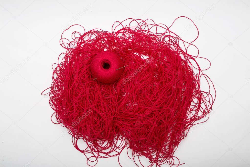 A ball of red thread and sewing needles on a white background