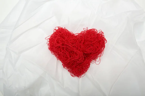 Heart of red threads on white silk background