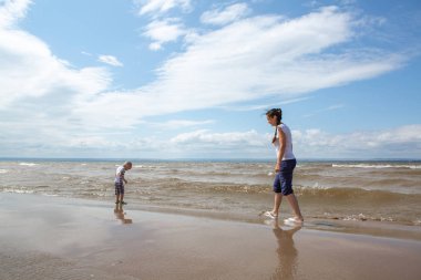 Çocuk annesiyle sahilde yürüyor.