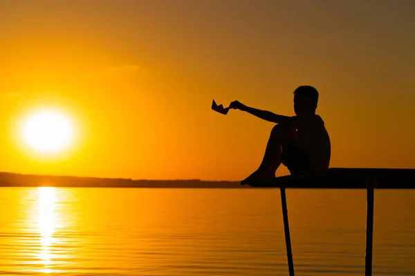 Niño Pequeño Sienta Puente Sostiene Barco Papel Mano Atardecer Río — Foto de Stock