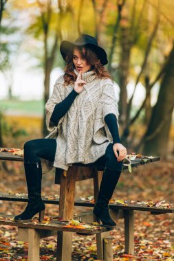 güzel bir kadının siyah şapkalı bir masaya oturur ve gizemli bir şekilde kenara parkta sonbaharda görünüyor