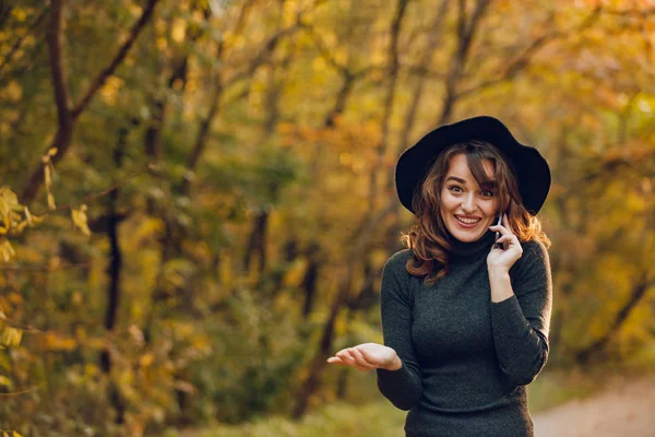 携帯電話で話しながら笑顔で美しい女性 陽気な女の子が秋の公園を散歩します — ストック写真
