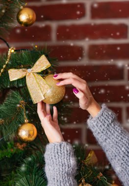 kadının ellerini kışın kar taneleri odada arka plan üzerinde bir yay-düğüm ile altın top tarafından Noel ağacı süsleyin. Yakın çekim