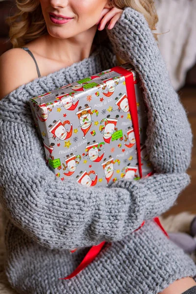 beautiful girl with make-up in a knitted dress holds a Christmas present. A woman in a warm dress looks perfect