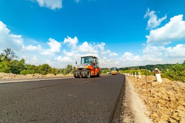 mavi gökyüzü arka plan üzerinde yeni bir asfalt üzerinde mühürleme ve yol yüzeyleri tesviye için makine özel milleri ile sürmek