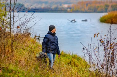 turist sırt çantası elinde tutuyor ve nehir kıyısında yüksek çimlere mesafe içine sonbaharda görünüyor