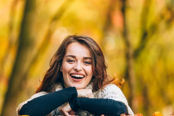 beautiful woman in warm clothes laughs in the park on the background of trees in the autumn. Close-up