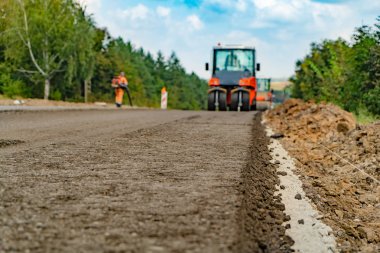 sıkıştırma asfalt yolda titreşimli silindir makinelerdir. Çalışan formundaki bir adam taş ve asfalt üfleyiciler kullanarak açılan çukurlar kalıntıları dışarı havaya uçurur. Yolların yama
