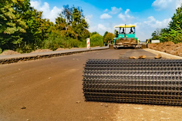 roll of reinforced mesh lays on the road on the background of professional equipment for the repair of roads. Close-up