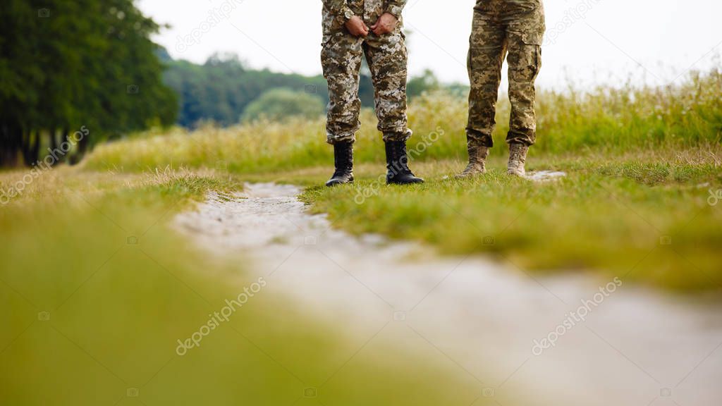 view of the legs of two men in military uniforms in boots near the pathway in the field on the background of nature. Close-up
