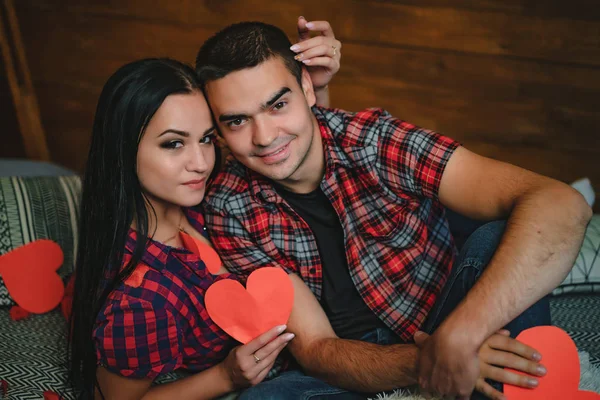 couple in love in checkered shirts sit in the studio with paper origami in the shape of hearts. Valentine\'s Day. Close-up.