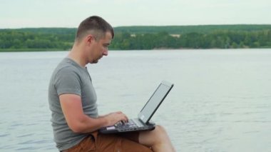 Dizüstü bilgisayar ile ahşap bir iskele üzerinde oturan yakışıklı adam