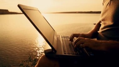 Nehrin yanında bir tepenin üstüne dizüstü bilgisayar kullanan adamın elleri. Güzel yaz günbatımı