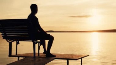 Bir bankta oturan bir kişi ile bir göl üzerinde huzurlu günbatımı