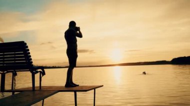 Fotoğrafçı çekimi sırasında günbatımı manzara resmini. Günbatımında nehirde yüzme insan silüeti