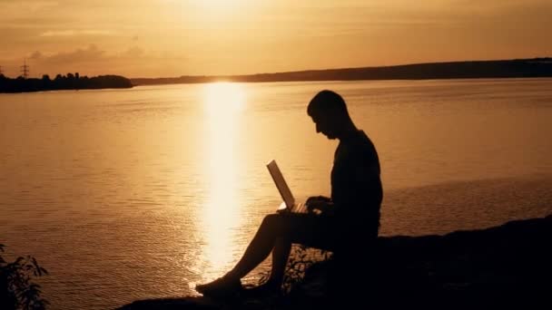 在山顶上的日落 背景下 男人坐在笔记本电脑上工作 — 图库视频影像