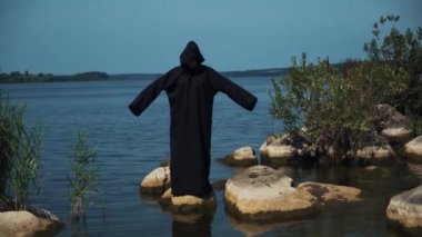 Kadın şeytan siyah pelerin ve kaputa taş Nehri yakınında. Halloween kılık.