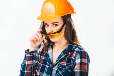 Gözlük tutan kask bina ile güzel bir model. Genç güzel kız ile koruyucu gözlük ve turuncu kask kameraya beyaz arka plan üzerinde görünüyor. Yakın çekim