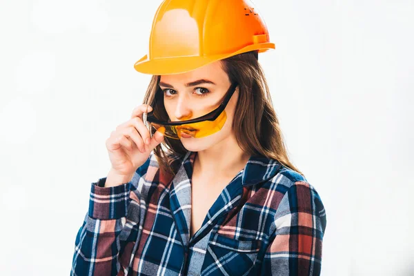 Gözlük tutan kask bina ile güzel bir model. Genç güzel kız ile koruyucu gözlük ve turuncu kask kameraya beyaz arka plan üzerinde görünüyor. Yakın çekim