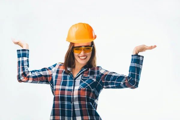 Happy young girl in blue and red shirt, glasses and orange protective helmet. Beautiful smiling woman in building helmet showing balance with her hands on white background.