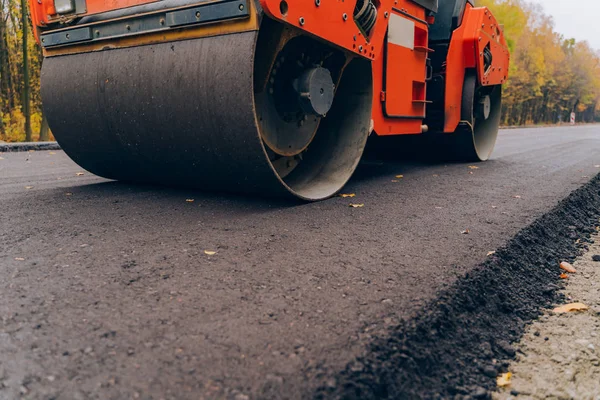 道路工事中のアスファルト舗装機を操作する作業者 新規の道路建設現場で働いてロード ローラーで表示を閉じる — ストック写真