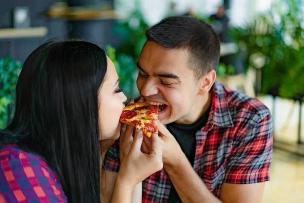 Lovely young couple in t-shirts sitting in a restaurant sharing slice of pizza. Close up photo of young couple eating tasty pizza together in pizzeria.