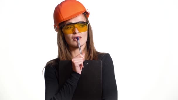白い背景に硬い帽子の若い女性建設労働者 魅力的な女性ビルダーとともにノートパッド手で決定を行います — ストック動画