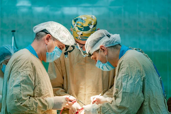 Concentrated surgeons in medical clothes with masks and magnifying glasses performing operation in operational room. Professional doctors making surgery operation.
