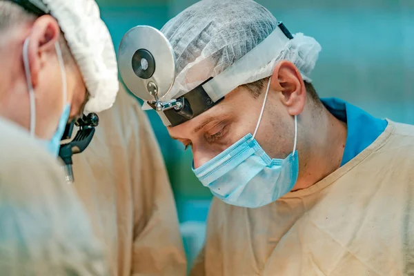 Concentrating surgeons in masks and magnifying glasses are performing operation in a hospital. Surgeon doctors in a medical clothes. Close-up