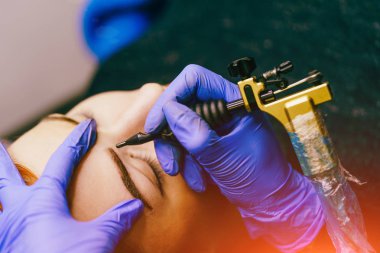 Profesyonel kalıcı uygulama kaslar üzerinde güzellik salonu dövme için bir araç ile telafi. Kadının yüzündeki kaş dövme yapma güzellik uzmanı.