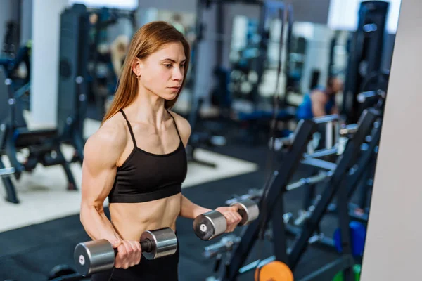 强壮的运动女子在黑色运动穿上升肌肉与哑铃在健身房 健身女孩与完美的身体在健身房有一个训练 — 图库照片
