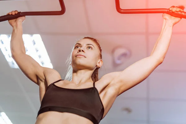 强壮的肌肉发达的女孩拉自己在天花板背景上的横杆 美丽的健身妇女在酒吧进行腹部锻炼 — 图库照片