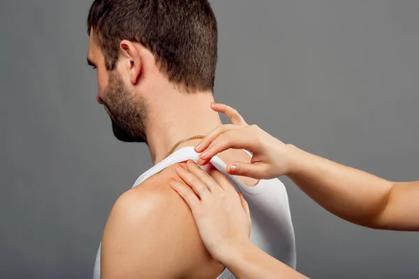 Doctor's hands examine the man with shoulder pain on gray background. Health concept. Hands of a woman checks mans back. Close-up