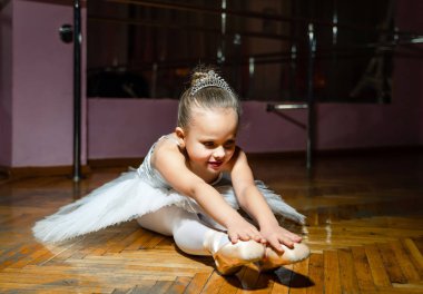 Çekici genç balerin ahşap katta oturan pointe ayakkabılarını uzanan beyaz tutu giyiyor. Küçük kız Studio egzersizleri yapıyor