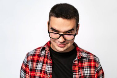 İyi görünümlü şık gözlük içine beyaz izole kamera üzerinde seyir kırmızı ve beyaz gömlekli bir adam. Genç erkek gülümseyen ve gözlüklü kameraya bakıyor. Yakın çekim