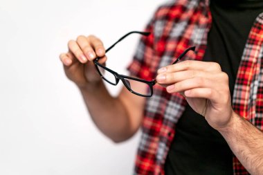 Parlak siyah çerçeve üzerinde beyaz izole ile moda gözlük gözlük tutan kareli gömlekli adam. Genç adam elinde modern gözlük