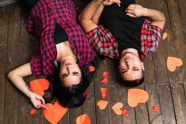 Mutlu Sevgililer çift üstten görünüm ahşap zemin üzerinde kırmızı kağıt yürekleri kameraya bakarak yalan söylüyor. Güzel romantik çift birçok küçük kalpler ile. Sevgililer günü