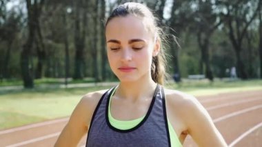 Spor giyimli genç bir bayan atletizm antrenmanından sonra sahada dinleniyor.