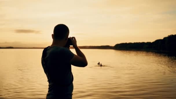 Mannen Med Kamera Händerna Gör Ett Foto Floden Bakgrunden Sunset — Stockvideo