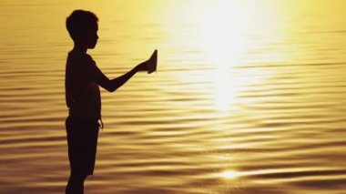 küçük çocuk bir kağıt uçak günbatımında elinde tutuyor. Bir çocuk elini gökyüzü ve akşam sokakta origami ile çalış kadar kaldırdı