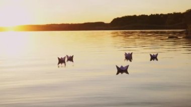 altı origami tekne yelken akşam günbatımında gölün şeklinde. Kağıt tekne uzakta su akışı ile geliyor.