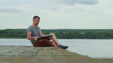 adam köprüde oturma ve yaz aylarında nehir arka plan üzerinde çalışmak için bir dizüstü açılış