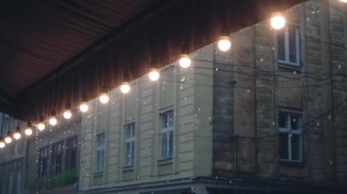yağmur damlaları Restoran çatısında lambalar Bina arka plan üzerinde dekoratif bir sıra ile düşer. Yağmur yağıyor