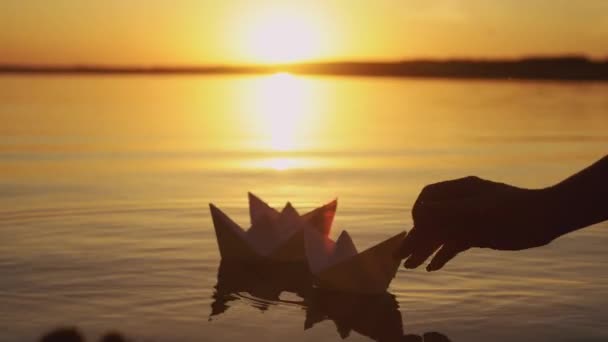 人間の手は 日没で湖に手作り紙船を始めています 船の形の折り紙が夕方には水に泳いでいます — ストック動画