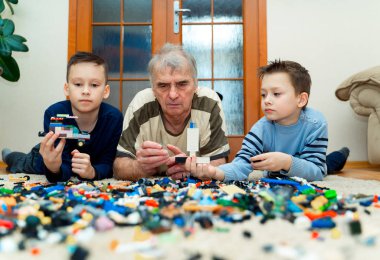 Dedesi onun torunları yerde yatarken ve cam kapı arka plan üzerinde evde lego tuğla ile inşa ile. Eski ve yeni nesil
