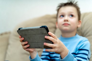 Bir kanepede oturan ve bir yana seyir sırasında PC tablet tutan Chlid. Çocuğun elleri ile bir kablosuz tablet üzerinde arka plan bulanık.